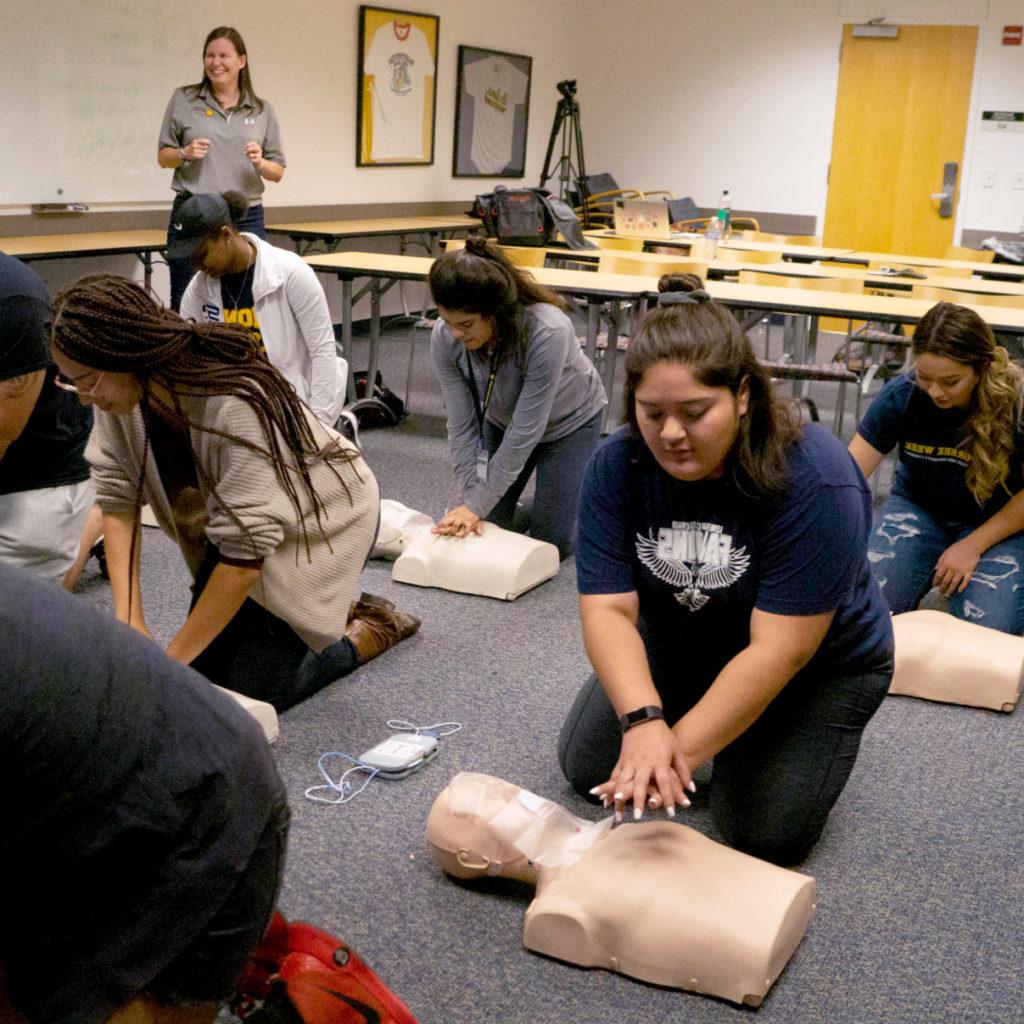 Students on the floor in front of a mannequin during a CPR class.