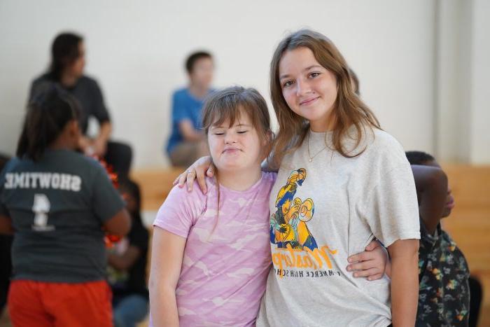 Two students share a hug side-by-side while posing for a photo.