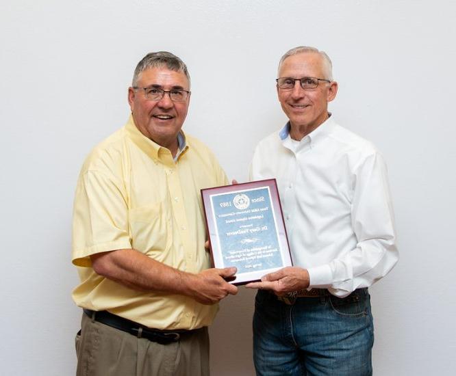 Award recipient and Dr. Harp face the camera with a white backdrop behind them. They both have one hand on a framed award.