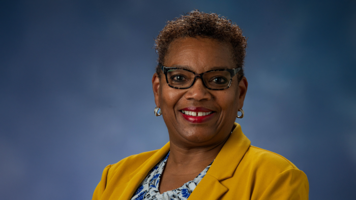 Professional photo of Dr. Sharon Ross wearing a gold blazer against a mottled blue background.